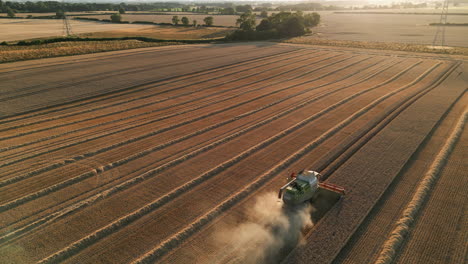 Erstellung-Einer-Drohnenaufnahme-Eines-Claas-Mähdreschers-Bei-Sonnenuntergang-Zur-Goldenen-Stunde-Mit-Orangenstaub-Und-Meist-Geerntetem-Feld-Großbritannien