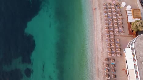 Nice-aerial-view-of-a-beach-with-turquoise-waters,-umbrellas,-and-posidonia,-at-sunset,-Albania