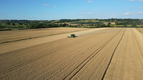 Establishing-Drone-Shot-of-Green-John-Deere-Combine-Harvester-Harvesting-Driving-Towards-Camera-on-Sunny-Day-UK