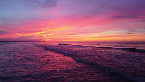 Aerial-dolly-out-revealing-the-softness-of-the-waves-passing-over-the-sea-in-an-epic-and-incredible-pink-and-yellow-sunset