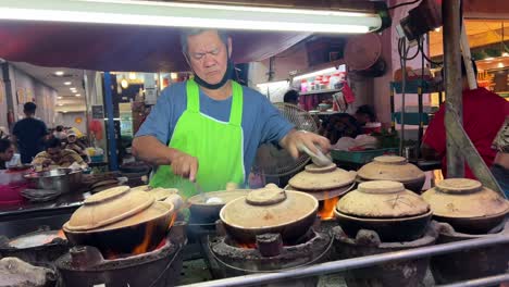 Puesto-De-Comida-Callejera,-Hombre-Malasio-Cocinando-En-Ollas-De-Barro-En-La-Calle-Kuala-Lumpur-Por-La-Noche