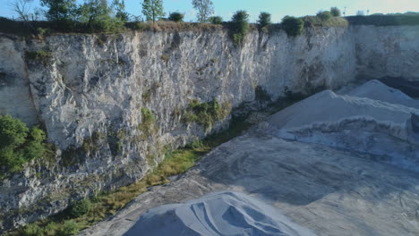 Drone-Shot-of-Small-Openpit-Limestone-Quarry-with-Heaps-of-Gravel-and-White-Cliffs-with-Small-Trees-on-top-in-Yorkshire-UK