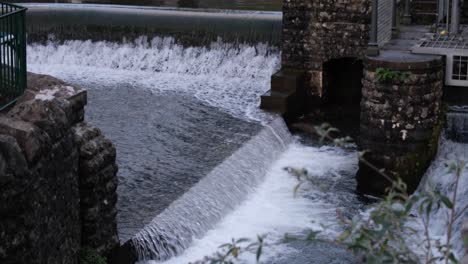 People-visiting-the-popular-village-of-Cheddar-with-Cheddar-Gorge-and-Yeo-River-with-beautiful-water-weir-on-the-Mendip-Hills-in-Somerset,-England