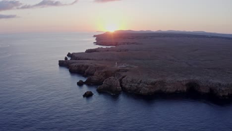 Long-aerial-approach-and-tilt-up-towards-Punta-Nati-Lighthouse-in-Menorca-Spain-at-sunset
