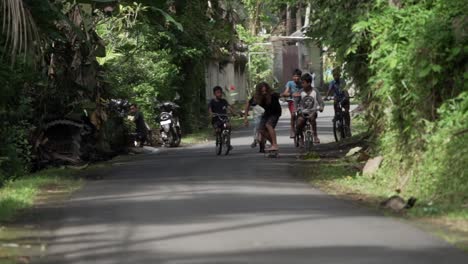 Slow-motion-shot-of-foreign-tourist-skating-down-the-road-followed-by-Indonesian-kids-riding-bikes