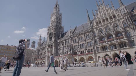 Full-shot-of-people-walking-and-enjoying-the-weather-in-front-of-a-cathedral-in-Munich,-Germany-on-a-sunny-day,-captured-with-a-handheld-camera