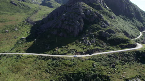 Aerial-pullback-shot-of-a-van-on-an-adventure-in-northern-Norway-on-a-highway-along-the-mountainous-coastline-near-the-remote-village-of-Nyksund