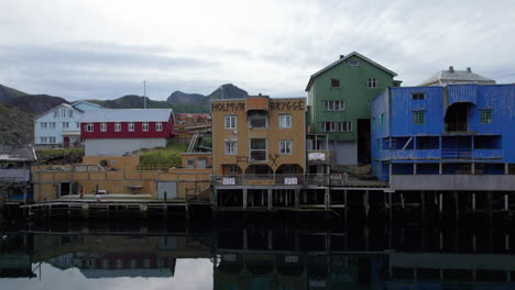 Aerial-dolly-forward-view-of-colorful-buildings-on-a-pier-along-the-the-shore-with-calm-water-on-an-overcast-day