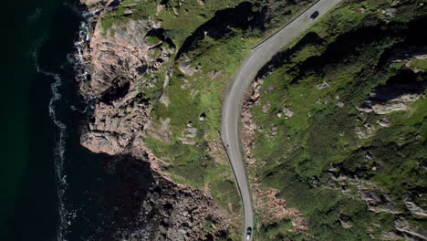 Aerial-top-down-following-shot-of-a-car-driving-on-the-most-dangerous-coastal-road-in-Norway-to-Nyksund
