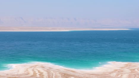 Surreal-landscape-view-of-the-Dead-Sea-in-Rift-Valley-of-Jordan,-with-white-salty-quicksand-coastline-and-turquoise-rippled-salty-water