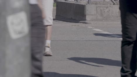 Handheld-shot-of-people-crossing-a-street-in-summer,-mostly-showing-legs-and-feet-in-a-documentary-style-with-the-subjects-in-focus