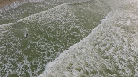 Establishing-aerial-birdseye-view-of-a-man-engaged-in-kitesurfing,-overcast-winter-day,-high-waves,-extreme-sport,-Baltic-Sea-Karosta-beach-,-drone-shot-moving-forward