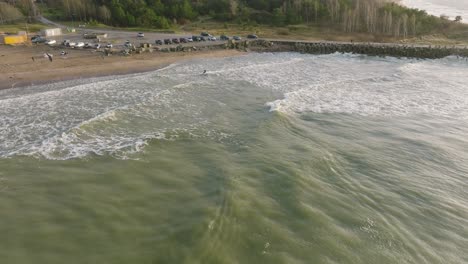 Establishing-aerial-view-of-a-man-engaged-in-kitesurfing,-overcast-winter-day,-high-waves,-extreme-sport,-Baltic-Sea-Karosta-beach-,-drone-shot-moving-forward