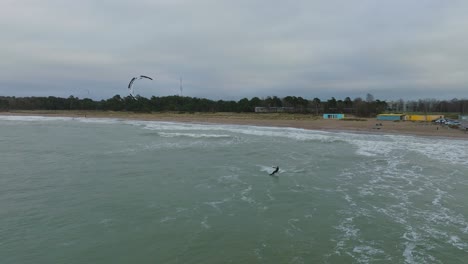 Erstellung-Einer-Luftaufnahme-Eines-Mannes,-Der-Kitesurfen-Betreibt,-Bewölkter-Wintertag,-Hohe-Wellen,-Extremsport,-Ostsee-Karosta-Strand,-Drohnenschuss,-Der-Sich-Vorwärts-Bewegt