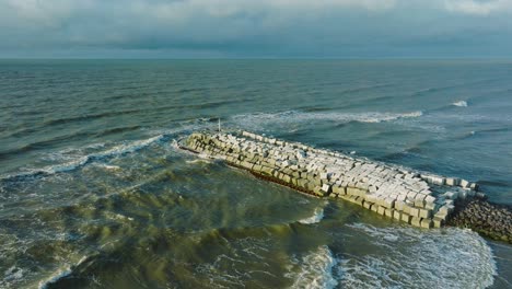 Aerial-establishing-view-of-protective-stone-pier-with-concrete-blocks-and-rocks-at-Baltic-sea-coastline-at-Liepaja,-Latvia,-strengthening-beach-against-coastal-erosion,-distant-orbiting-drone-shot