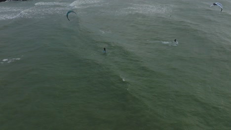 Establecimiento-De-Una-Vista-Aérea-De-Pájaros-De-Un-Grupo-De-Personas-Dedicadas-Al-Kitesurf,-Día-De-Invierno-Nublado,-Olas-Altas,-Deporte-Extremo,-Playa-De-Karosta-Del-Mar-Báltico,-Tiro-De-Drones-Avanzando