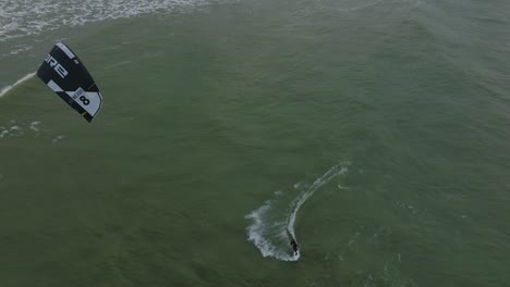 Establishing-aerial-view-of-a-man-engaged-in-kitesurfing,-overcast-winter-day,-high-waves,-extreme-sport,-Baltic-Sea-Karosta-beach-,-drone-birdseye-shot-moving-forward