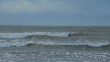 Man-engaged-in-kitesurfing,-overcast-winter-day,-high-waves,-Baltic-Sea-Karosta-beach-,-slow-motion,-wide-shot