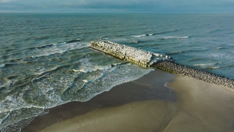 Aerial-establishing-view-of-protective-stone-pier-with-concrete-blocks-and-rocks-at-Baltic-sea-coastline-at-Liepaja,-Latvia,-strengthening-beach-against-coastal-erosion,-wide-drone-shot-moving-forward