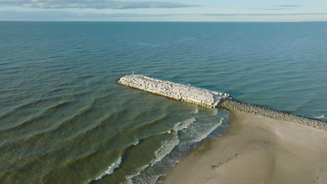 Aerial-establishing-view-of-protective-pier-with-concrete-blocks-and-rocks-at-Baltic-sea-coastline-at-Liepaja,-Latvia,-strengthening-beach-against-coastal-erosion,-drone-shot-moving-forward-tilt-down