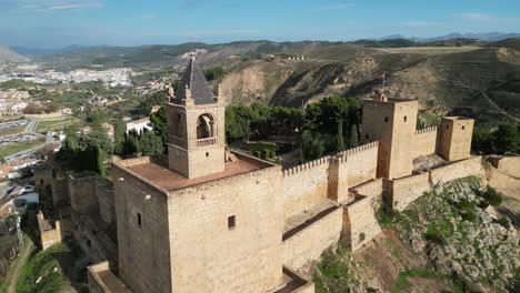 Antequera-Fortress-and-Spanish-waving-flag-in-Andalusia,-Spain---Aerial-4k-Circling