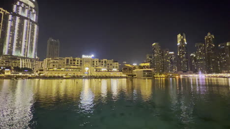 Super-wide-view-of-luxurious-restaurants-and-hotels-near-the-Dubai-fountain-reflection,-at-night
