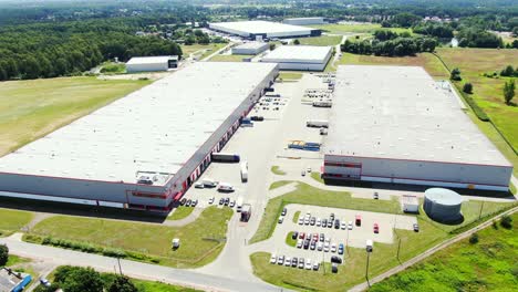 Aerial-Shot-of-Truck-with-Attached-Semi-Trailer-Leaving-Industrial-Warehouse-Storage-Building-Loading-Area-where-Many-Trucks-Are-Loading-Unloading-Merchandise