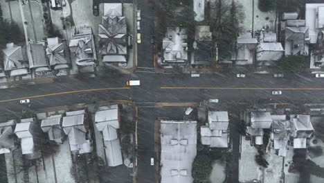 Aerial-tracking-shot-of-American-short-school-bus-driving-on-small-town-streets-during-snow-storm