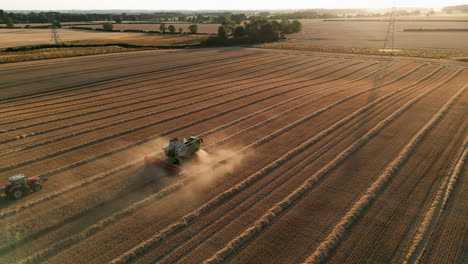 Establecimiento-De-Una-Toma-De-Drones-De-Una-Cosechadora-Claas-En-El-Polvo-Con-Un-Tractor-Y-Un-Remolque-A-La-Hora-Dorada-Del-Atardecer-En-El-Reino-Unido