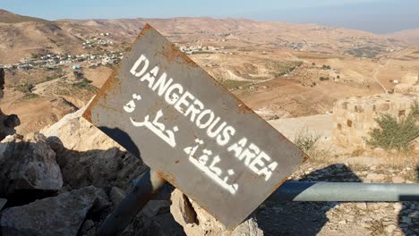 Warning-sign-with-dangerous-area-in-English-and-Arabic-overlooking-vast-desert-landscape-of-Jordan,-Middle-East