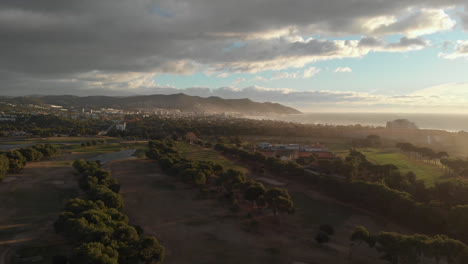 Eine-Drohne-Nimmt-Während-Der-Magischen-Goldenen-Stunde-Eine-Panoramaaufnahme-Eines-Nebligen-Grünen-Golfplatzes-An-Der-Küste-Auf