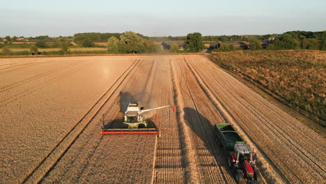 Front-On-Drone-Shot-De-La-Cosechadora-Claas-Con-El-Brazo-Fuera-Y-El-Tractor-Con-El-Remolque-Vacío-Conduciendo-A-La-Hora-Dorada-Del-Reino-Unido