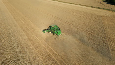 Fallende-Drohnenaufnahme-Des-Grünen-John-Deere-Mähdreschers,-Der-An-Einem-Sonnigen-Sommertag-In-Großbritannien-Staub-Sprüht