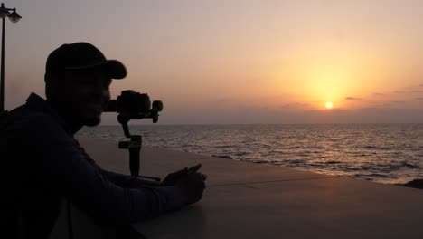 Silhouette-Des-Fotografen-Und-Der-Dslr-kamera,-Die-Den-Orangefarbenen-Sonnenuntergang-über-Dem-Ozean-Filmen