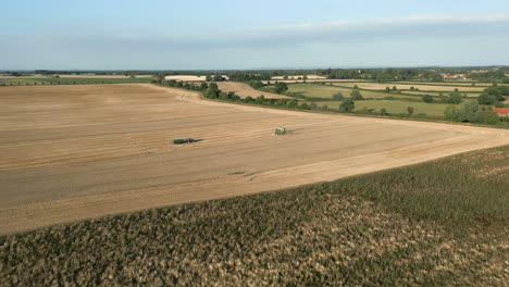 Weitwinkelaufnahme-Einer-Drohnenaufnahme-Von-Claas-Mähdrescher-Und-Traktor,-Die-Zur-Goldenen-Stunde-Am-Abend-Im-Vereinigten-Königreich-Auf-Dem-Feld-Arbeiten