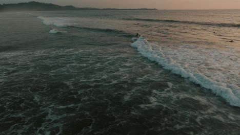 Surfer,-Die-Bei-Sonnenuntergang-Auf-Großen-Wellen-Am-Guanacaste-Beach-In-Costa-Rica-Reiten---Luftdrohnenaufnahme