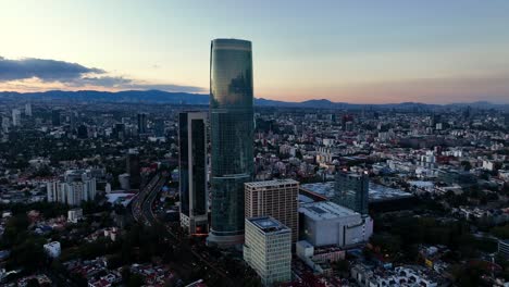 Aerial-view-away-from-the-Mitikah-tower,-dusk-in-Benito-Juárez,-Mexico---pull-back,-drone-shot