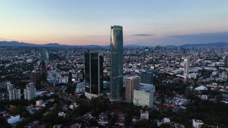 Mítikah-Tower-is-a-mixed-use-office-and-residential-tower,-colorful-evening-in-Benito-Juarez,-Mexico---Orbit,-aerial-view