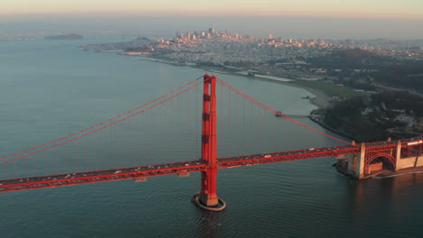 Wide-circling-aerial-shot-of-the-golden-gate-bridge-at-sunset-with-San-Francisco-skyline-in-the-background