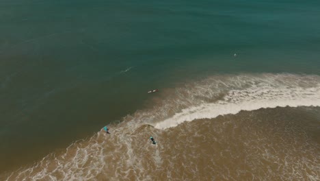 Surfers-Walking-Into-The-Sea-To-Surf-In-Guanacaste-Beach-In-Costa-Rica---aerial-drone-shot