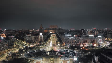 Toma-Aérea-De-Hiperlapso-De-Tráfico-En-Carretera-Con-Rotonda-Y-Edificio-Del-Parlamento-De-Bucarest-En-Segundo-Plano-Por-La-Noche