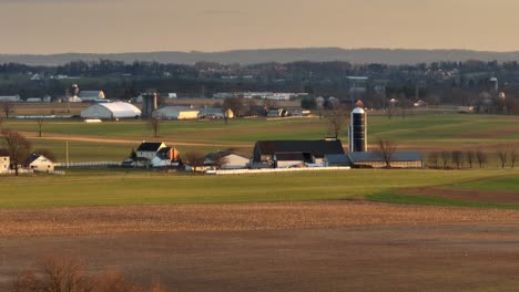 Long-aerial-zoom-of-Amish-farm-in-Lancaster,-Pennsylvania-during-golden-hour-sunset-in-winter
