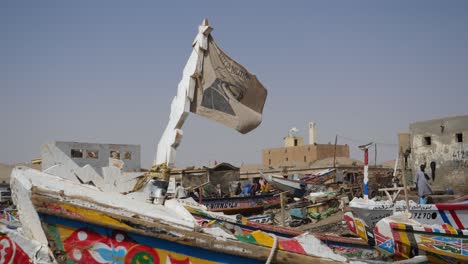 Flagge-Mit-Gezeichnetem-Ibrahim-Niass-Gesicht,-Das-Auf-Fischerboot-Auf-Mauretanischem-Ozeanufer-Und-Strand-Von-Nouakchott-Schwenkt