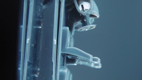A-tiny-model-metal-sample-skeleton-of-a-car-on-a-rotating-stand-with-studio-lights,-vertical-macro-close-up-shot,-4K-video,-silver-wheels,-black-tires,-doors-and-windows,-plastic-seats