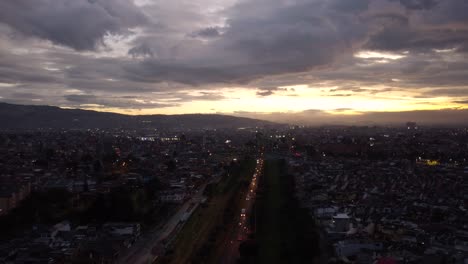 Drone-shot-above-Colombia's-capital-city-Bogota,-during-golden-hour,-orange-sky-and-calm-clouds,-lively-city