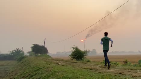 Slow-motion-shot-of-man-jogging-on-rural-path-near-Industry-smokestack