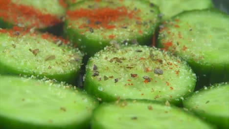 A-macro-close-up-shot,-falling-pepper-and-red-sweet-paprika-spice-grains-on-a-cut-slices-of-a-fresh-salted-green-cucumber,-slow-motion-4K-video