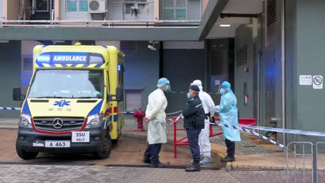 Ein-Polizist,-Gesundheitspersonal-Und-Ein-Krankenwagen-Werden-Vor-Einem-Gebäude-Gesehen,-Das-In-Einem-öffentlichen-Wohnkomplex-Abgeriegelt-Wurde,-Nachdem-Eine-Große-Zahl-Von-Bewohnern-In-Hongkong-Positiv-Getestet-Wurde