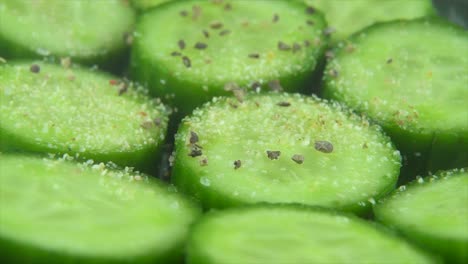 A-macro-close-up-shot,-falling-pepper-and-spice-grains-on-a-cut-slices-of-a-fresh-salted-green-cucumber,-slow-motion-4K-video