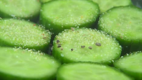 A-macro-close-up-shot,-falling-pepper-grains-on-a-cut-slices-of-a-fresh-salted-green-cucumber,-slow-motion-4K-video